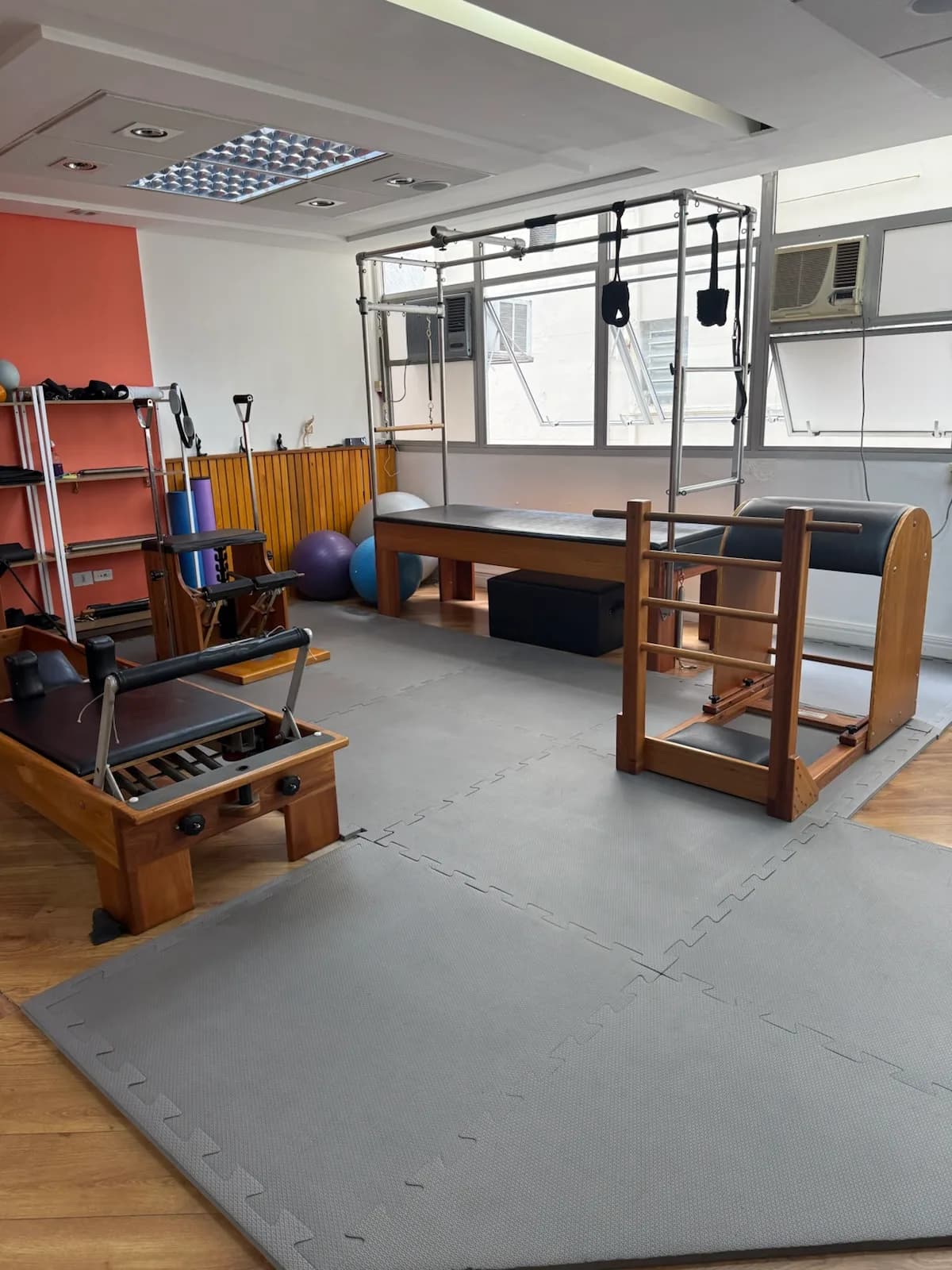Estúdio de pilates da unidade Consolação com cadillac, escada e barril, parede coral ao fundo.