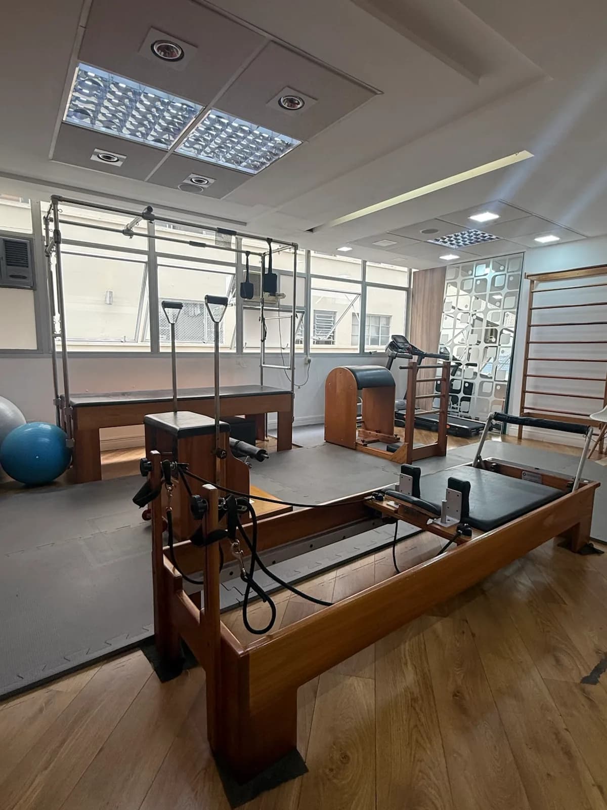 Estúdio de pilates da unidade Consolação iluminado por luz natural, com cadillac, cadeira e espaldar de madeira.
