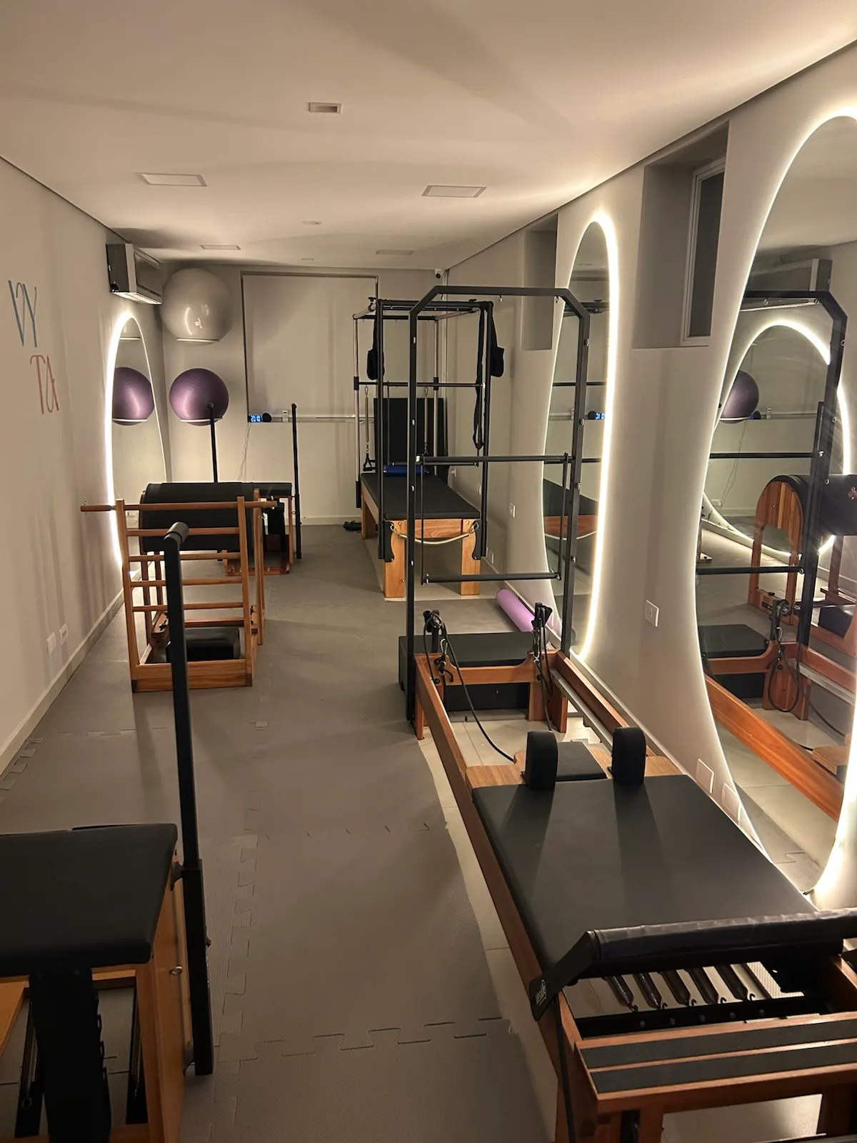 Corredor do estúdio de Pilates da Vyta em Pinheiros, com fileira de espelhos arqueados iluminados refletindo reformers e outros aparelhos