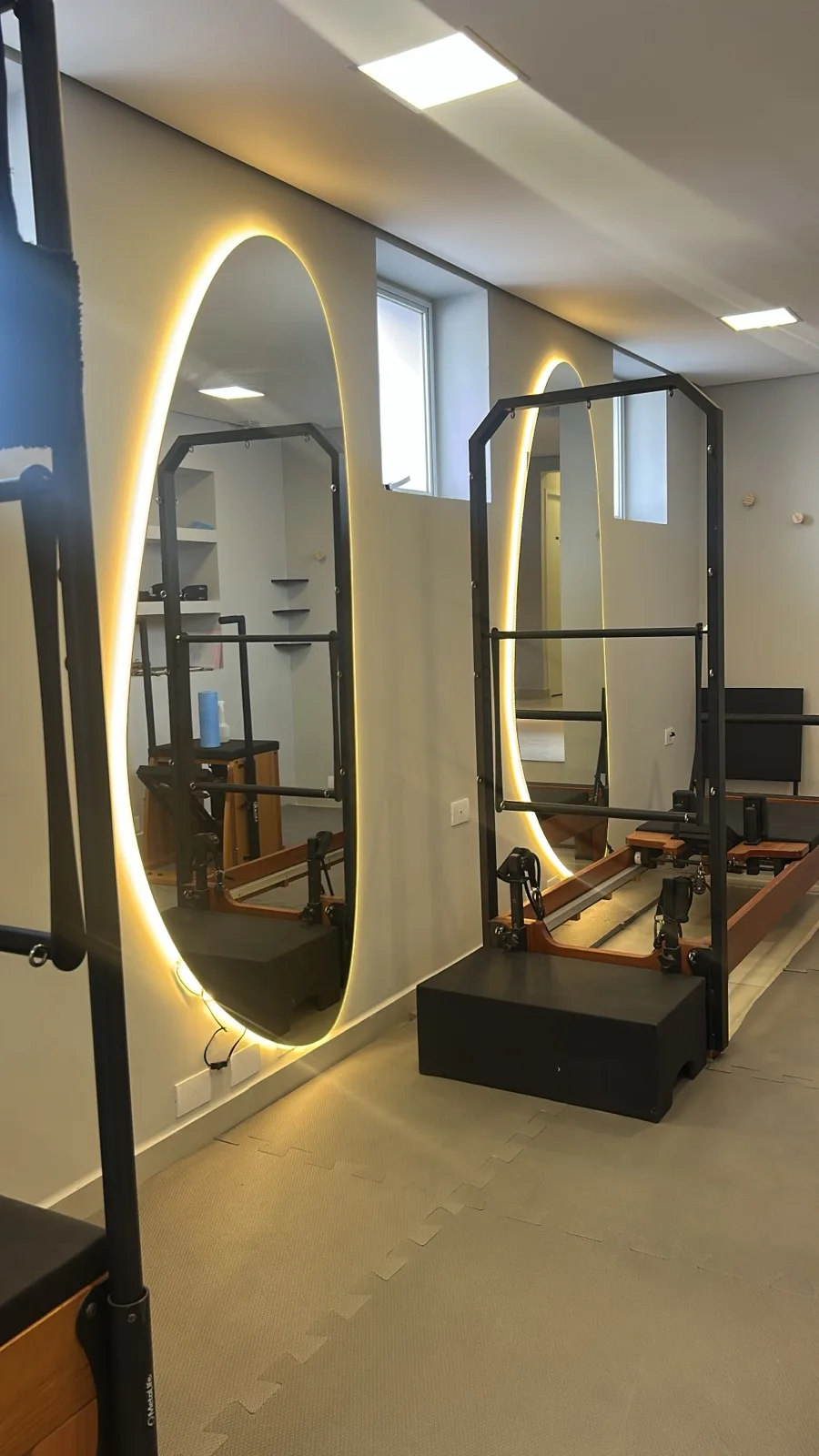 Detalhe do estúdio de pilates da unidade Pinheiros refletido em espelhos ovais retroiluminados.