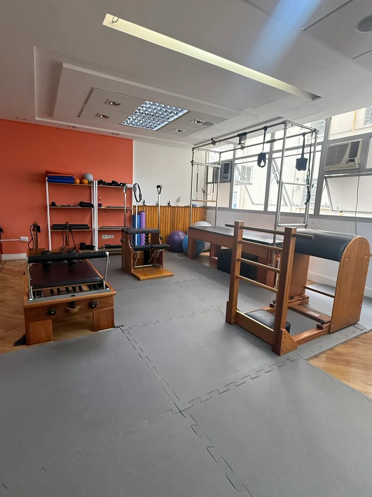 Reformer, cadillac e escada no estúdio de pilates da unidade Consolação, parede coral ao fundo.